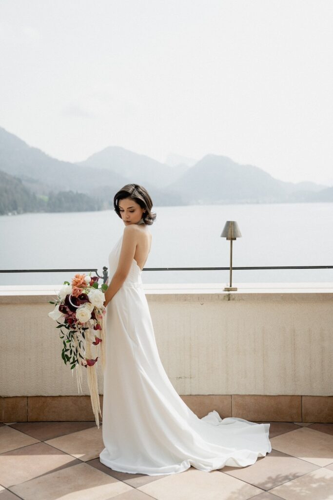 Die Braut steht auf der Terrasse mit Panoramablick über den Fuschlsee - Hochzeitsplanung in Österreich durch Münchner Wedding Planner