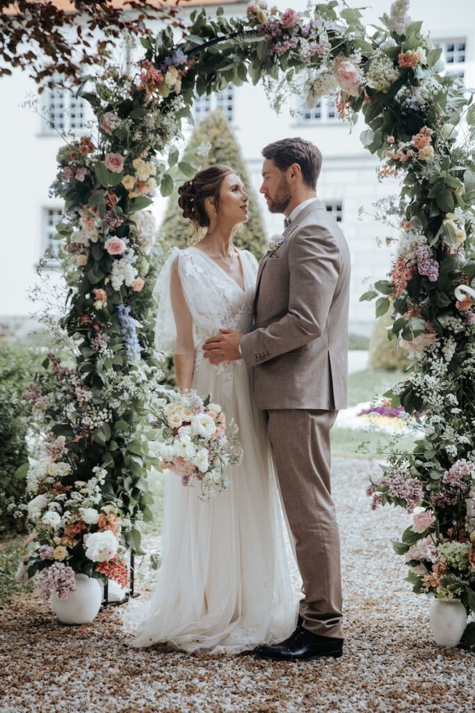 Brautpaar steht vor dem Traubogen - Hochzeit auf Schloss Lautrach begleitet von Glanz Hochzeiten Hochzeitsplaner aus München